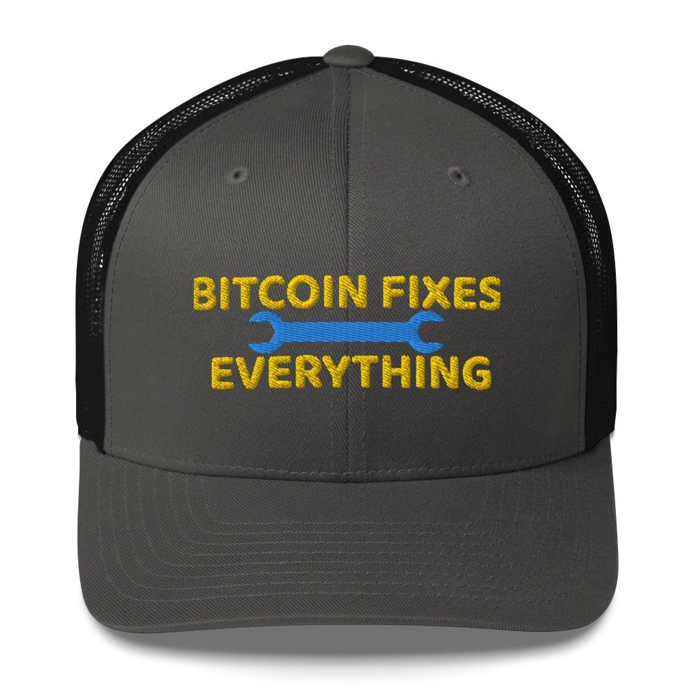 A black and gray UTXO Dreams trucker hat with the slogan "Bitcoin Fixes Everything" embroidered in bold yellow letters, accentuated by a blue and yellow wrench graphic on either side of the text.